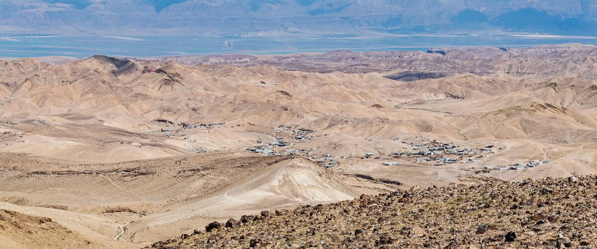 A desert landscape with a small settlement and distant mountains.