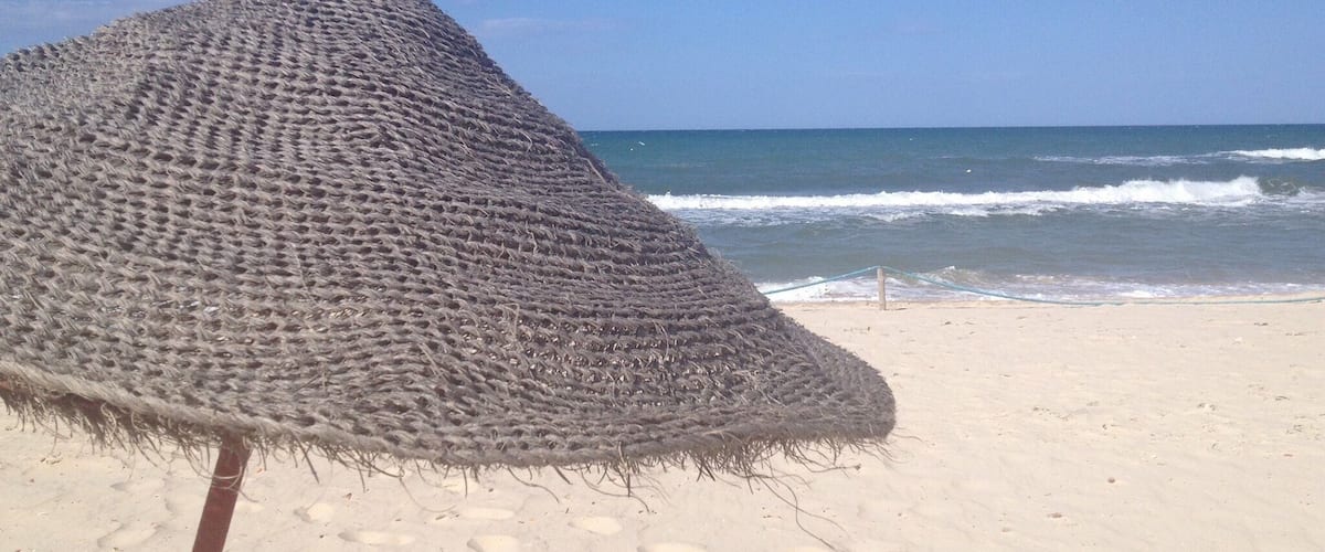 A beach with a thatched umbrella and ocean waves.