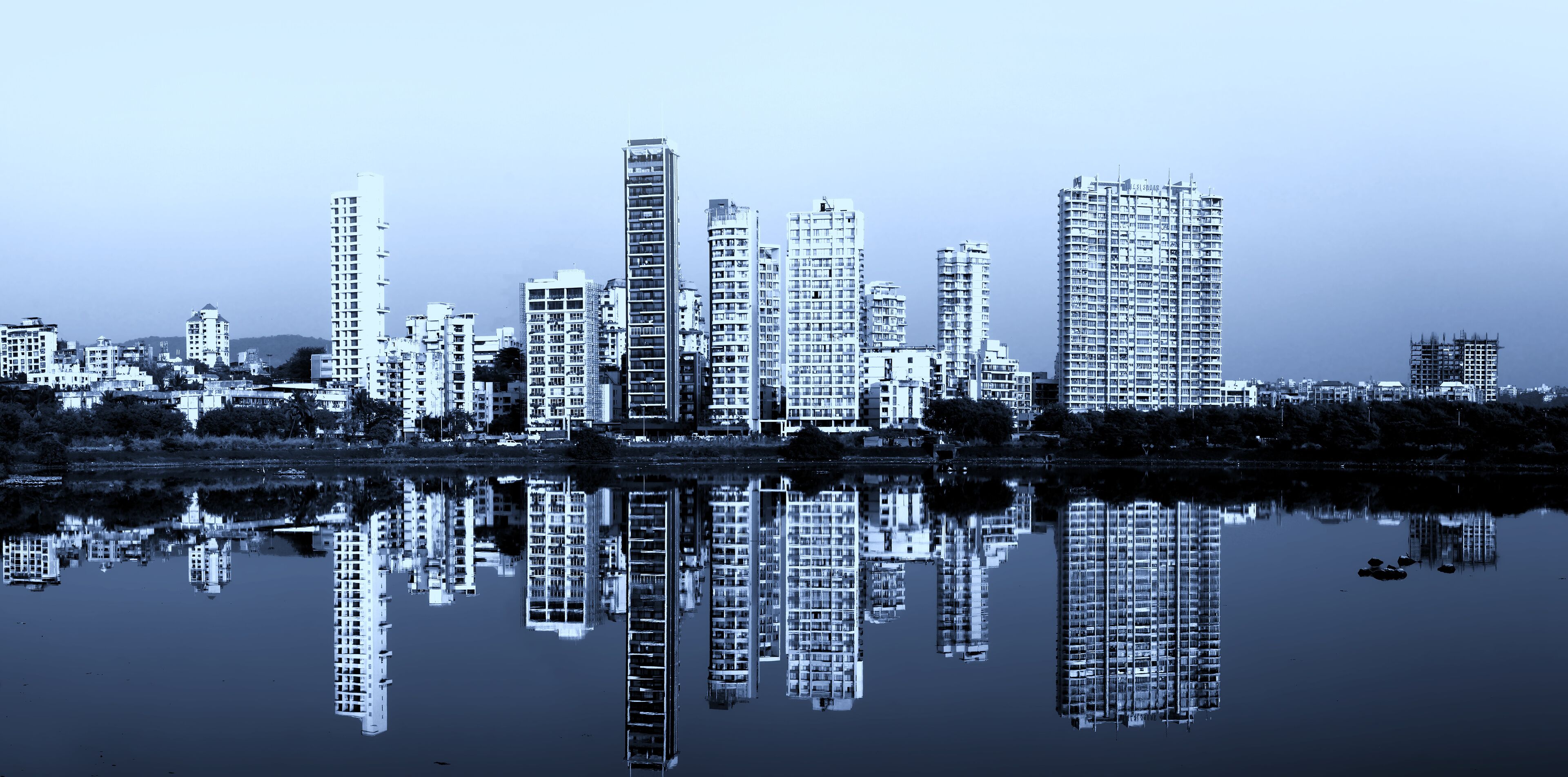A city skyline reflected in calm water, featuring high-rise buildings and a clear sky.