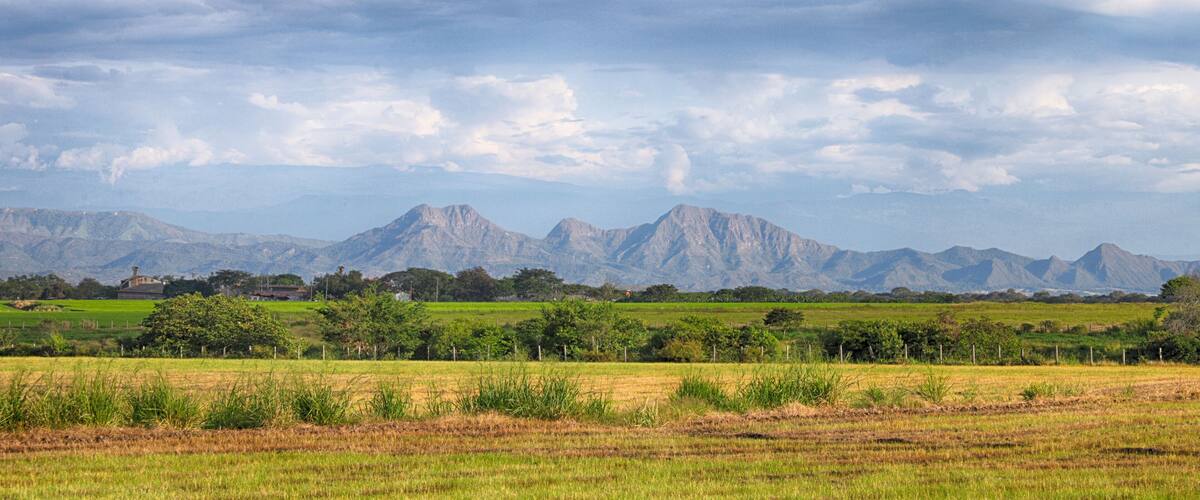 A mountainous landscape with green fields and a cloudy sky.