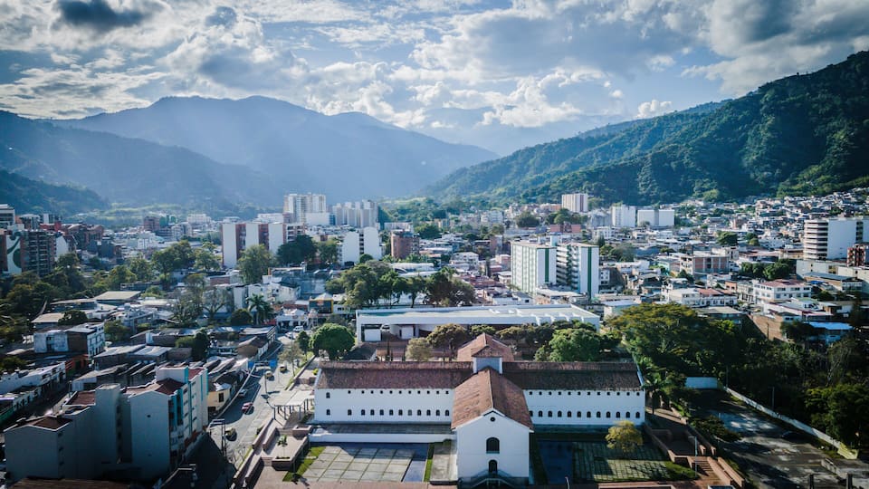 A cityscape with a prominent white church, surrounded by residential and commercial buildings, under a partly cloudy sky with mountains in the background.