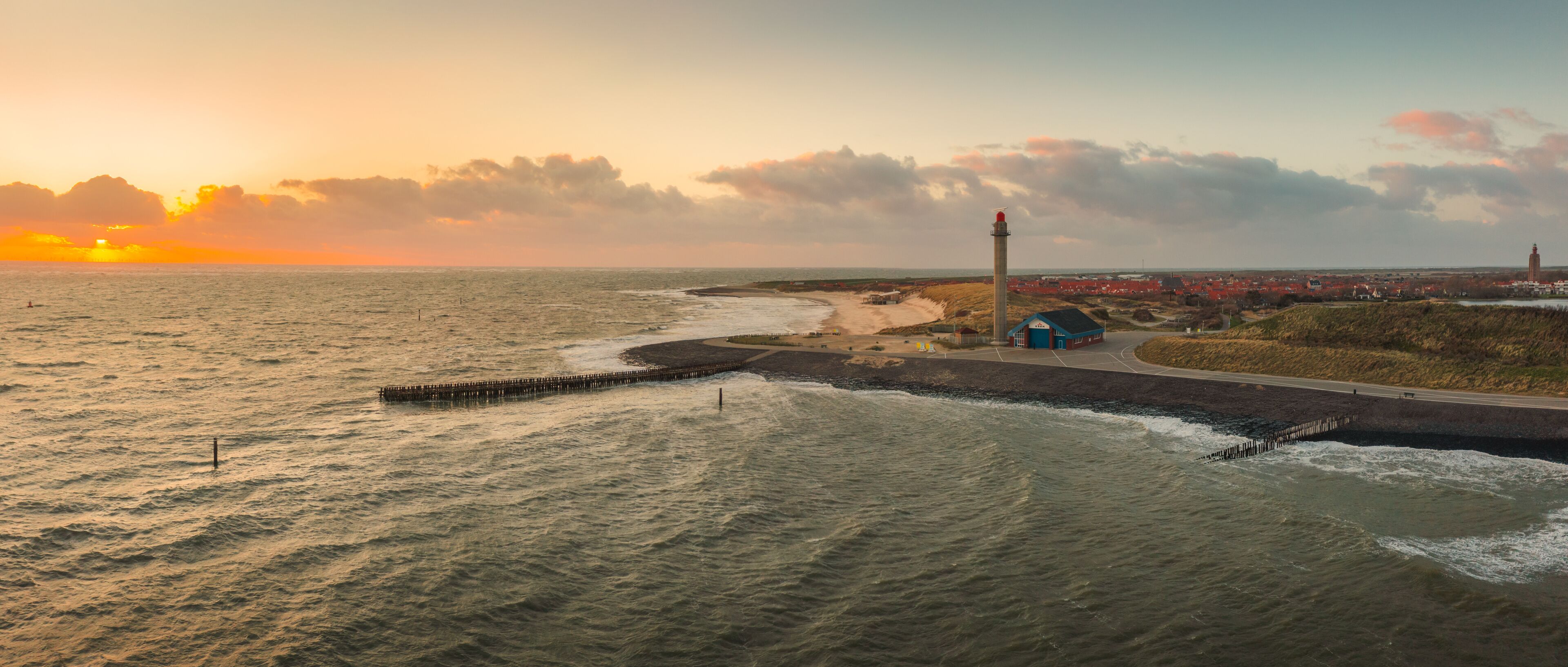 A coastal landscape with a lighthouse, beach, and a distant town.