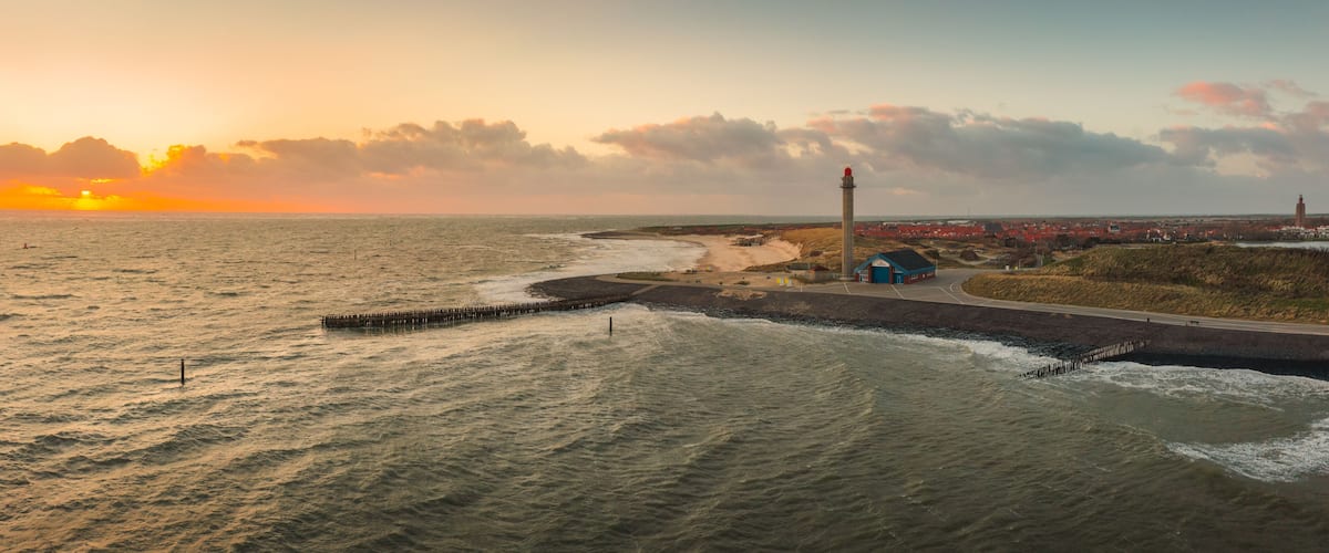 A coastal landscape with a lighthouse, beach, and a distant town.