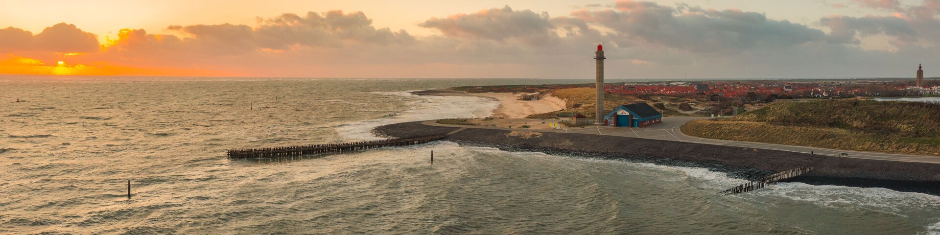 A coastal landscape with a lighthouse, beach, and a distant town.