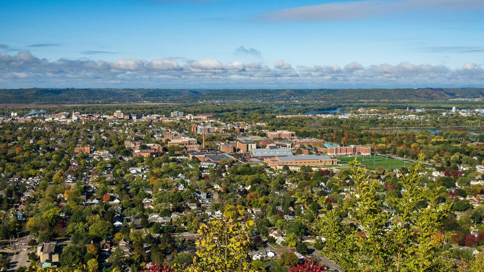 A cityscape with a mix of residential and commercial buildings, surrounded by greenery and a river.