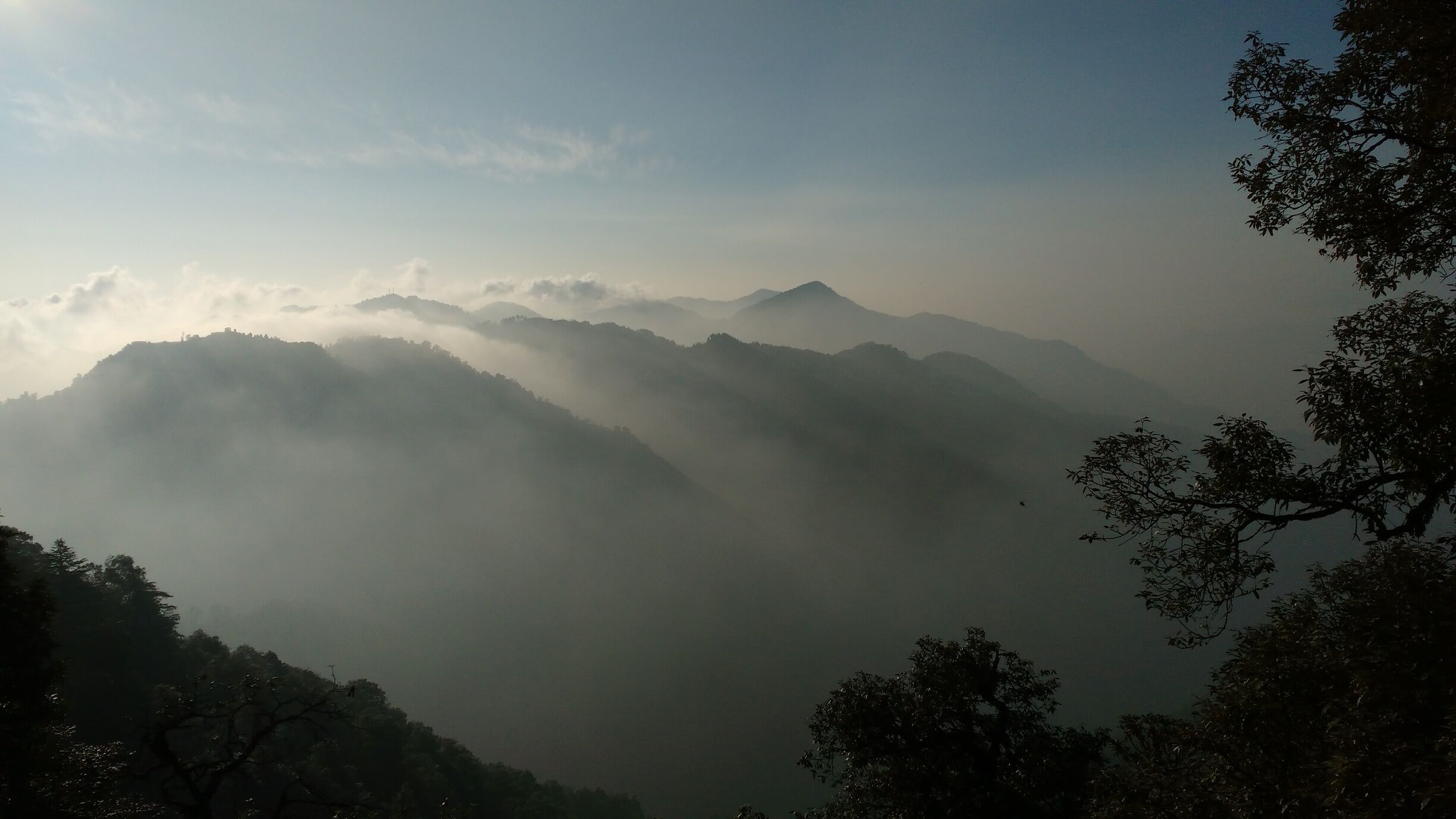 A mountainous landscape with mist-covered peaks and dense forest.