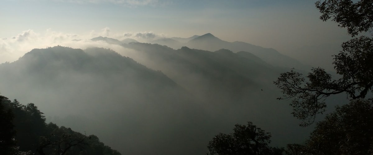 A mountainous landscape with mist-covered peaks and dense forest.