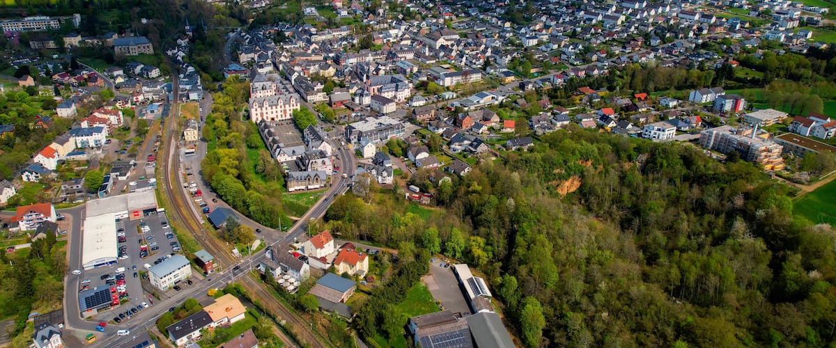 An aerial view of a town with a mix of residential houses, a central road, and surrounding green fields.