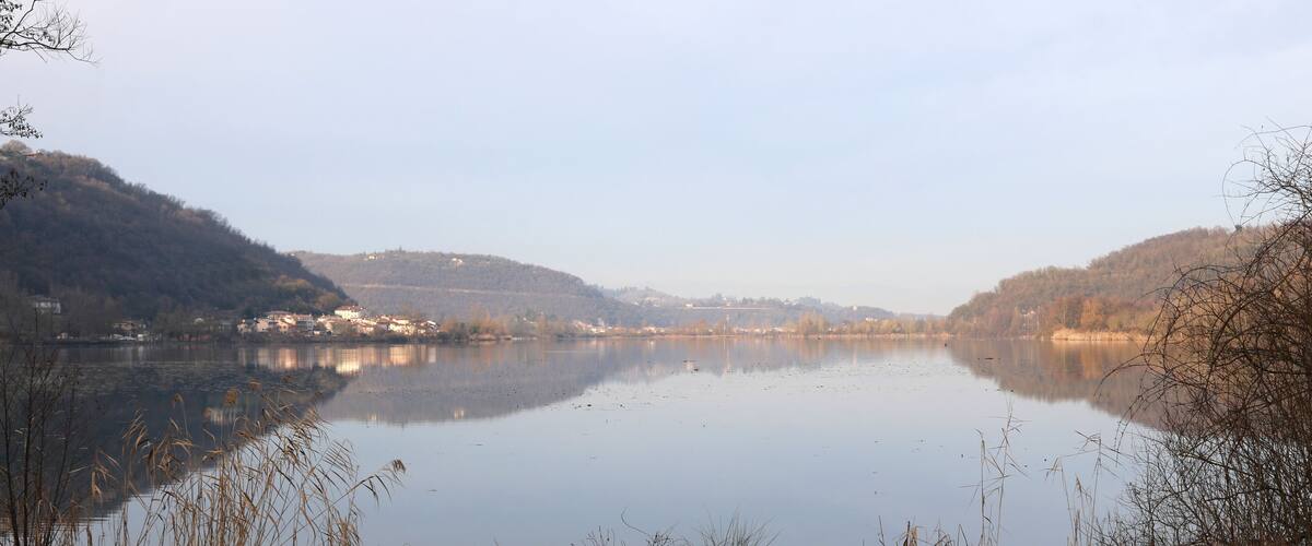 A calm lake with reflections of the surrounding hills and a small village in the distance.