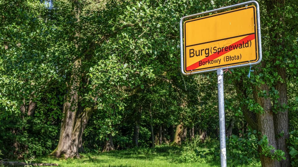 A yellow sign with black text indicating directions to Burg (Spreewald), Borkowy (Bota), and a red line.