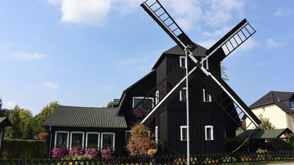 A black windmill with a white roof, surrounded by a wooden fence and colorful flowers.