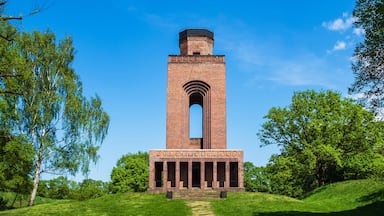 A tall brick tower with a central archway, surrounded by lush green trees and grass.