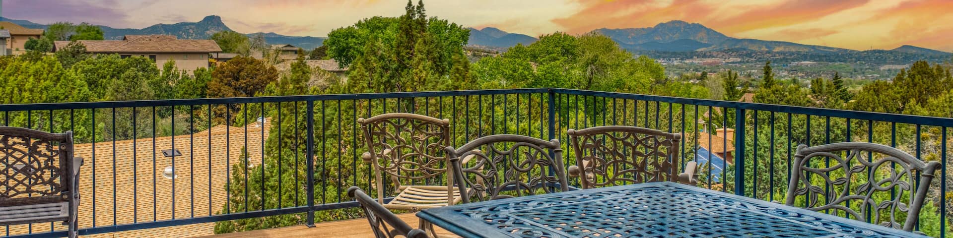 A patio with a table and chairs overlooking a scenic landscape with mountains and a sunset.