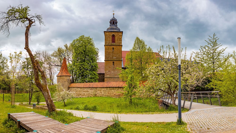 A church with a bell tower, surrounded by greenery and a paved walkway.