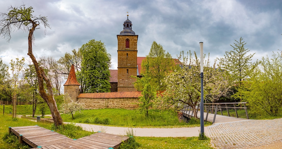 Eine Kirche mit einem Glockenturm, umgeben von Grünflächen und einem gepflasterten Weg.