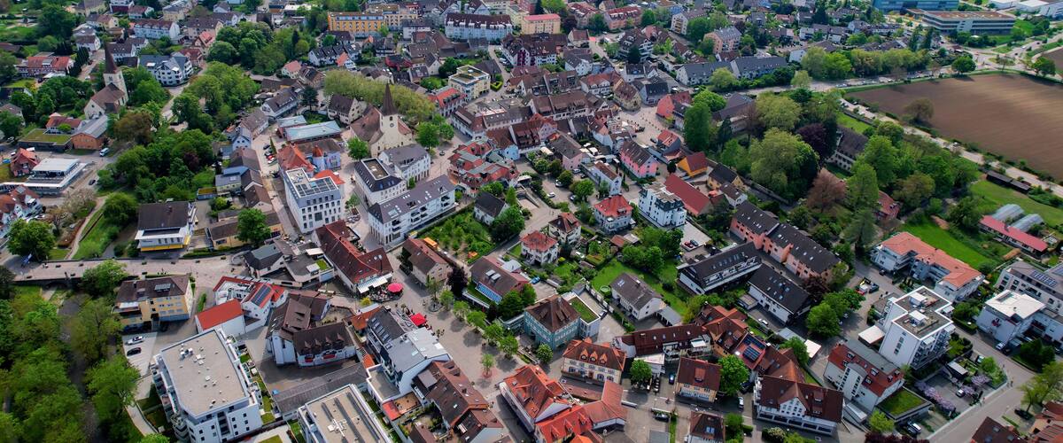 An aerial view of a densely populated town with a mix of residential and commercial buildings, surrounded by green fields and patches of farmland.