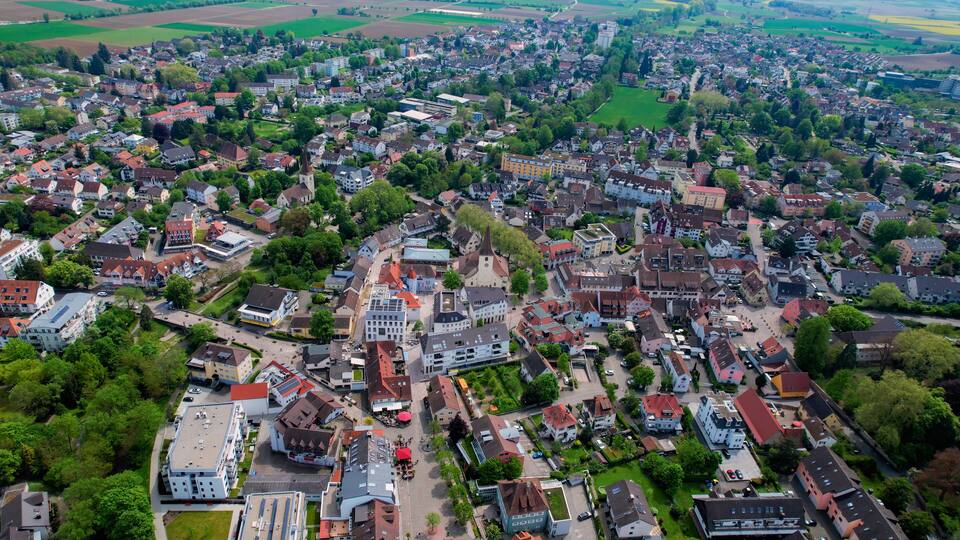 An aerial view of a densely populated town with a mix of residential and commercial buildings, surrounded by green fields and trees.