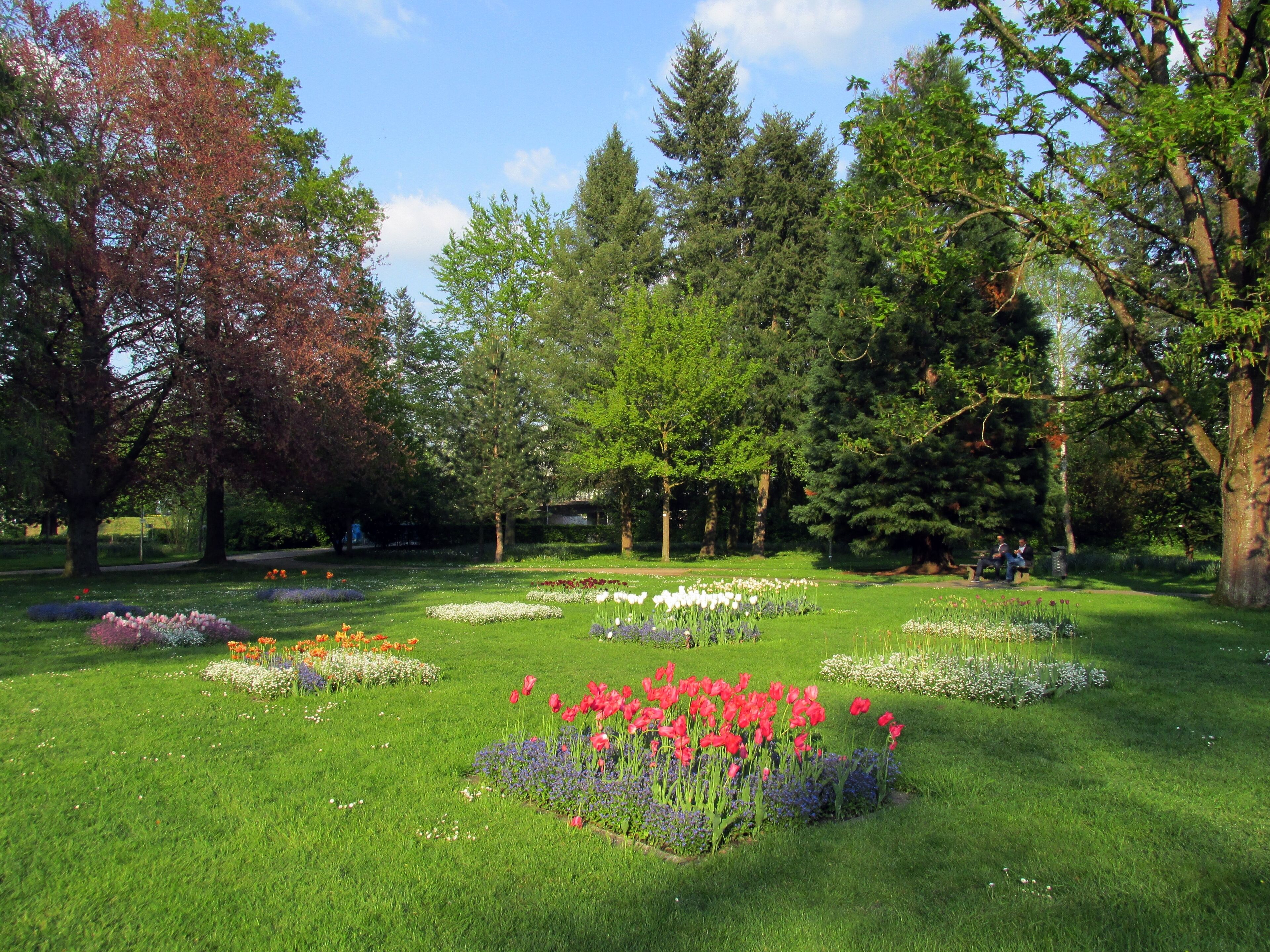 A park with various flower beds, trees, and a pathway.