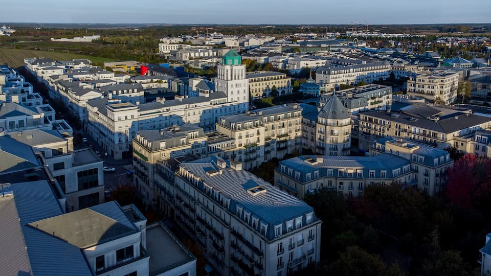 An aerial view of a cityscape with dense urban architecture, including a prominent green-roofed building and a red structure.