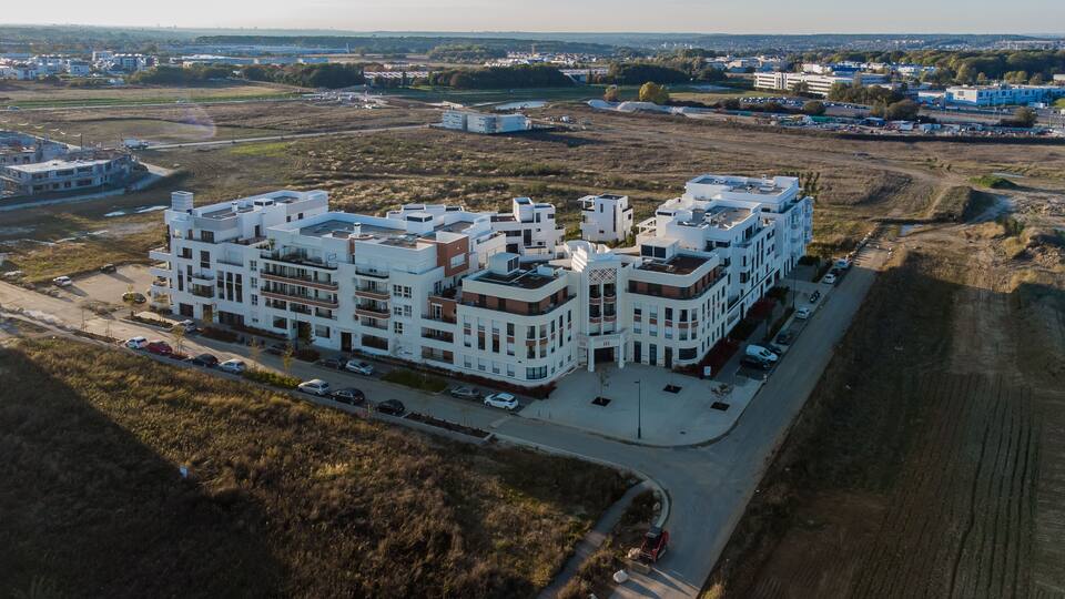 A large, multi-story residential building complex with a parking area in the foreground.