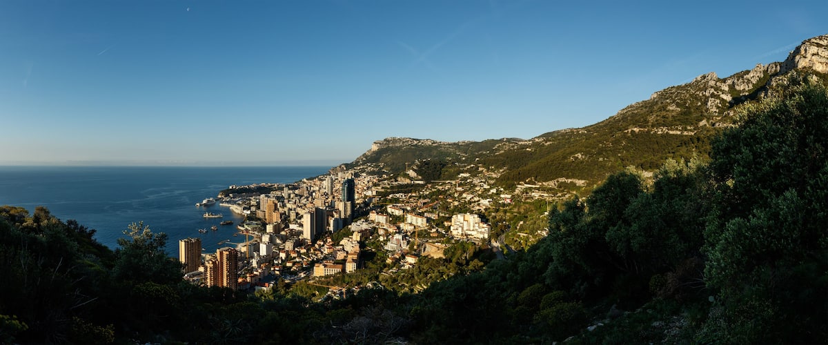 A coastal city with dense urban buildings, a harbor with boats, and a mountainous backdrop.