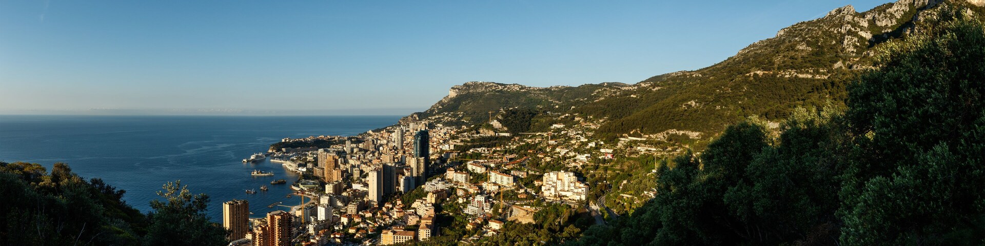 A coastal city with dense urban buildings, a harbor with boats, and a mountainous backdrop.