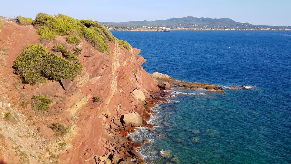 A coastal cliff with green vegetation and a clear blue sea.