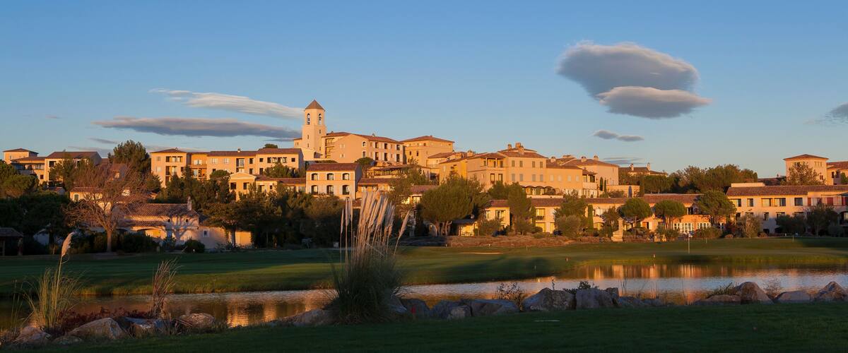 A coastal town with historic buildings, a church tower, and a golf course with a pond.