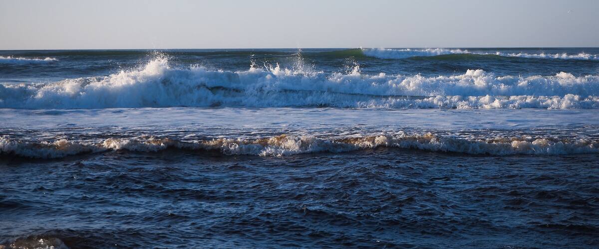 A coastal scene with waves crashing onto the shore under a clear sky.