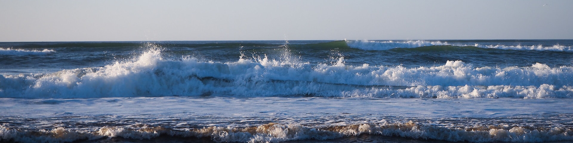 A coastal scene with waves crashing onto the shore under a clear sky.