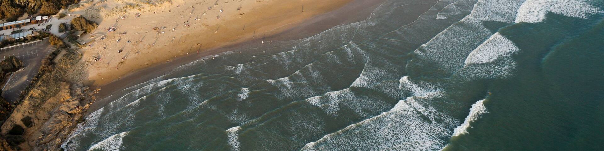 An aerial view of a coastal landscape with a sandy beach, a river flowing into the sea, and a forested area.