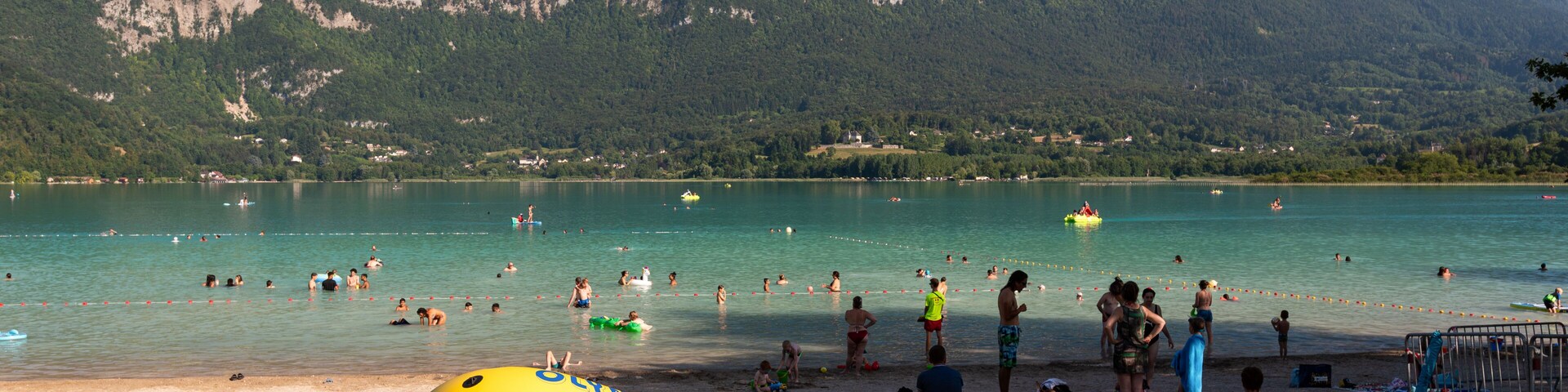 A lake with people swimming and a yellow raft on the grass.