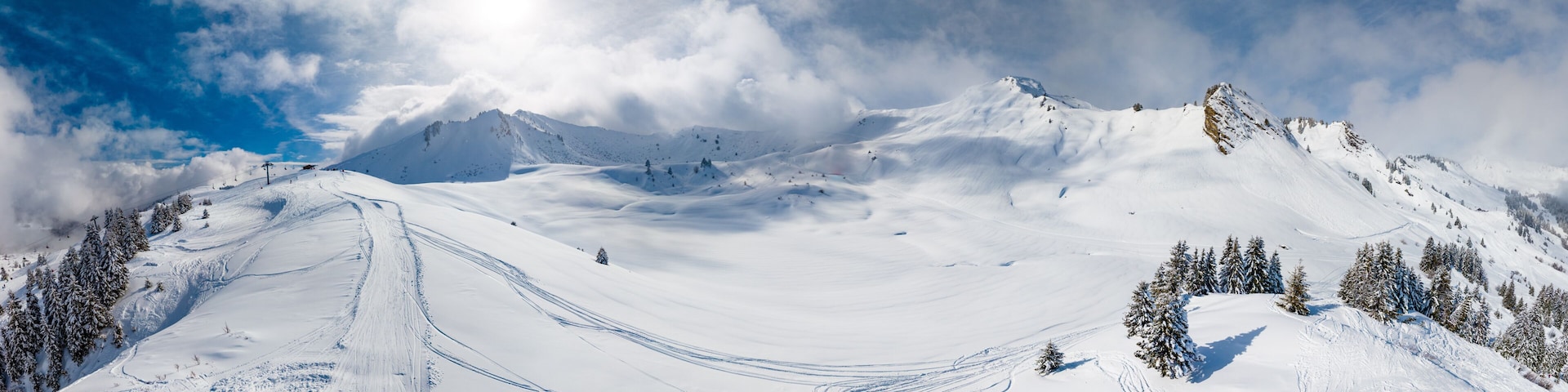 A snow-covered mountain landscape with ski tracks and evergreen trees.