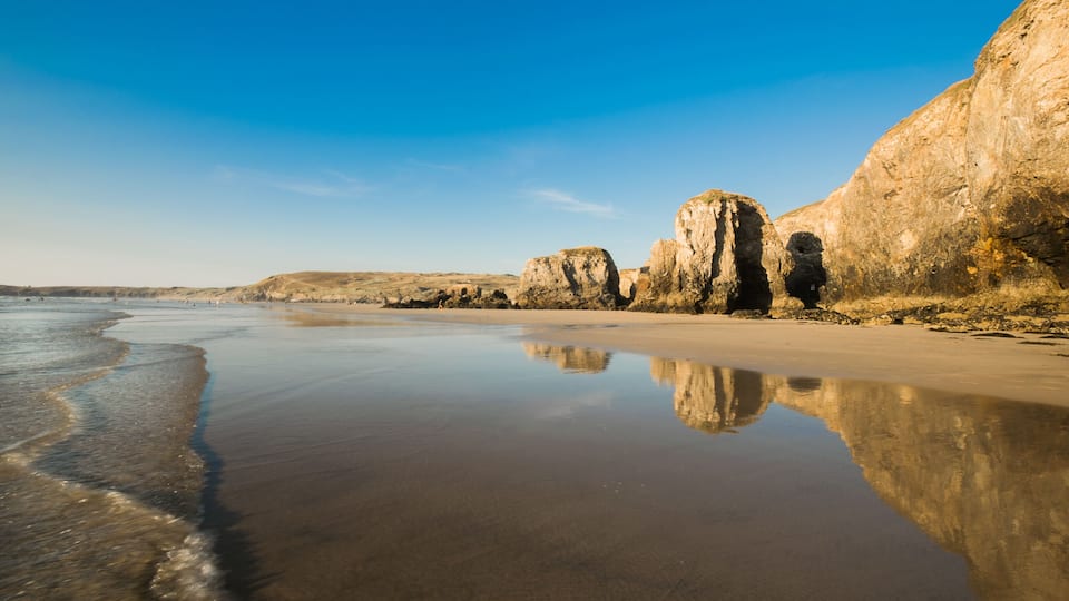 A beach with clear water reflecting the sky and rock formations.