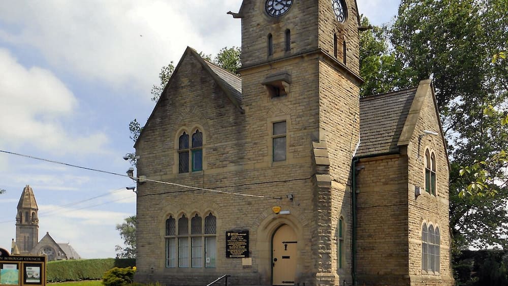 A historic church with a clock tower and a smaller tower, surrounded by greenery.