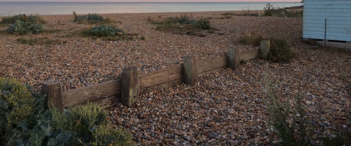 A pebbled beach with a wooden fence and a small white building.