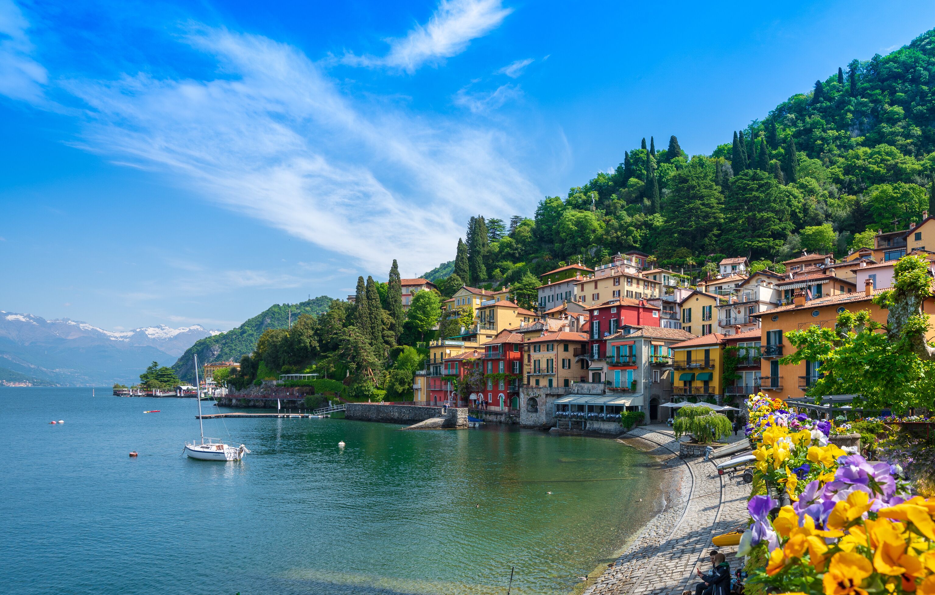 A lakeside town with colorful buildings, boats, and a mountainous backdrop.