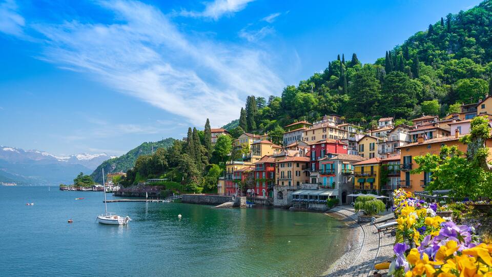 A lakeside town with colorful buildings, boats, and a mountainous backdrop.