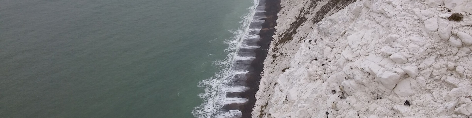 Eine Küstenklippe mit weißen Felsformationen und einem Leuchtturm in der Ferne.