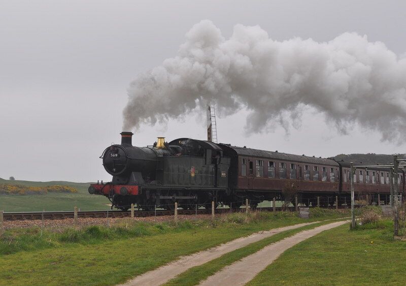 A steam locomotive with a chimney emitting smoke, traveling on a railway track.