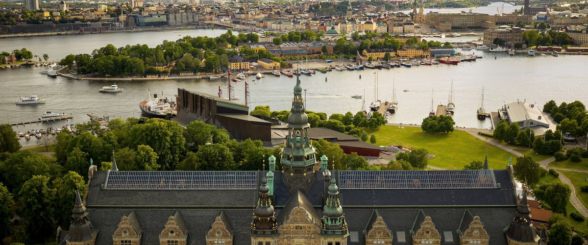A large historic building with ornate architecture, a river with boats, and a cityscape in the background.