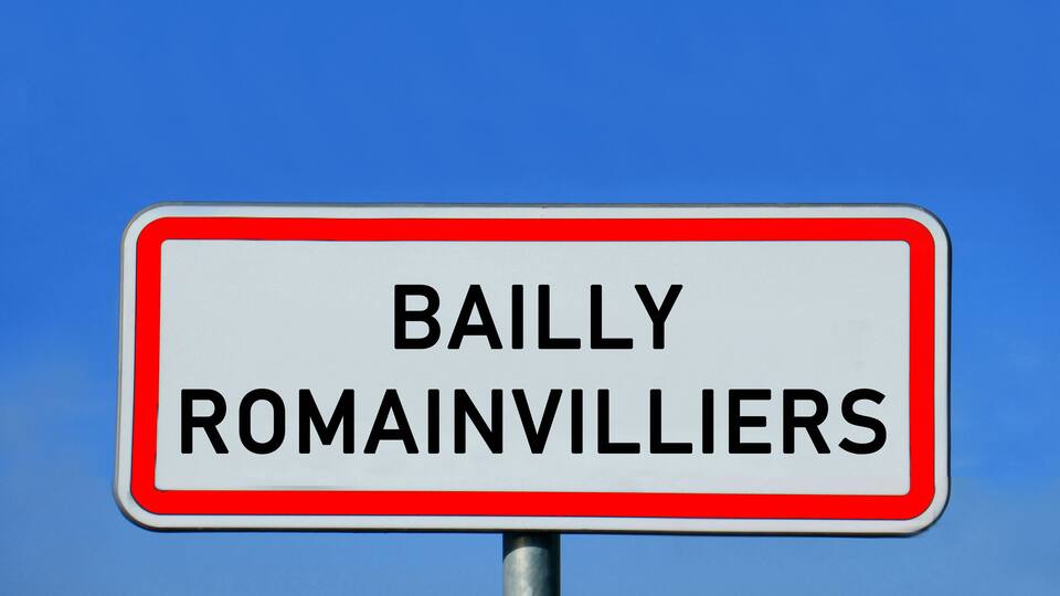 A sign with the text "BAILLY ROMAINVILLIERS" against a blue sky.
