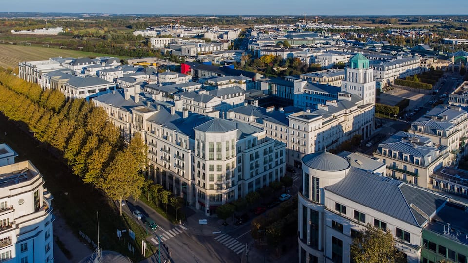 A cityscape with a prominent green-roofed building, a large white building with a dome, and a dense cluster of white buildings with blue roofs.