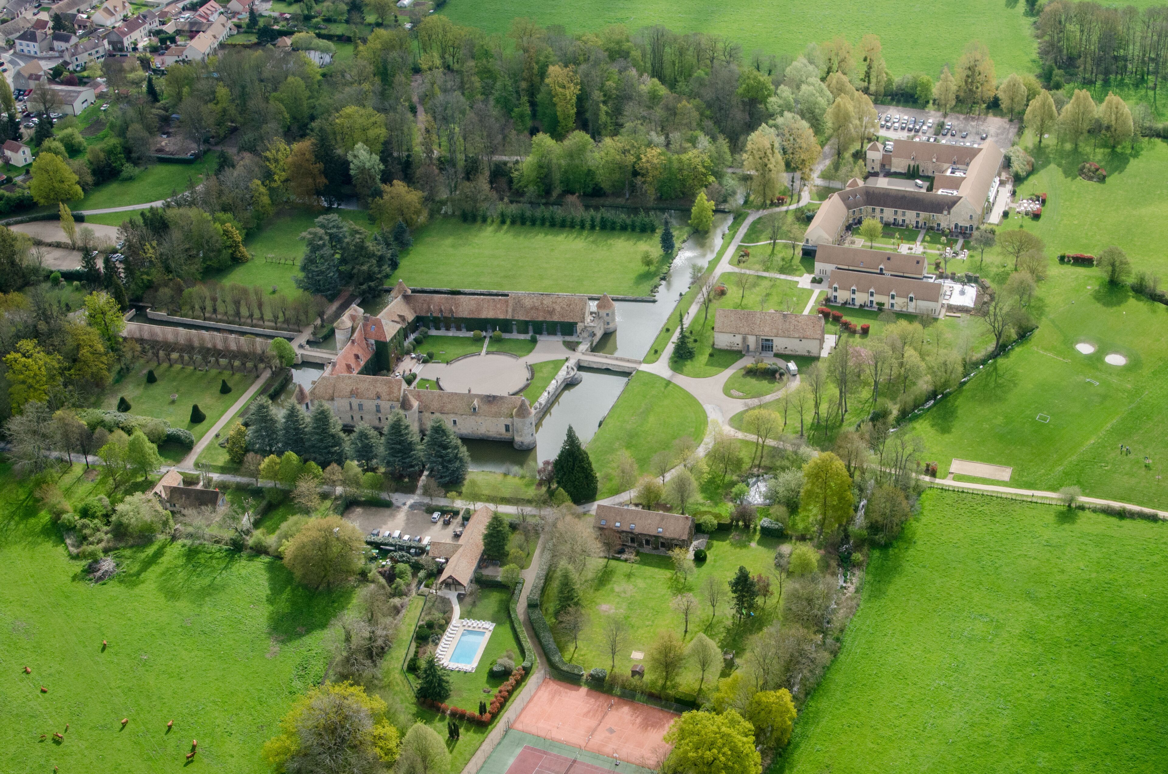 An aerial view of a large estate with a castle, tennis courts, and a river.