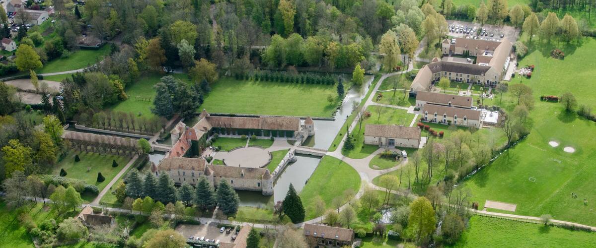 An aerial view of a large estate with a castle, tennis courts, and a river.