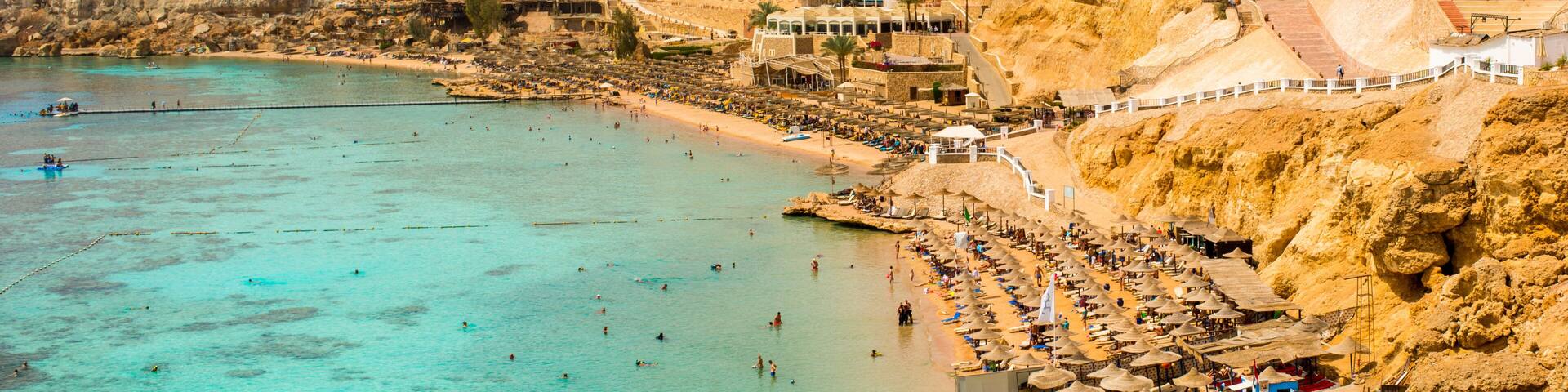 A coastal city with a beach, mountains in the background, and a mix of traditional and modern architecture.