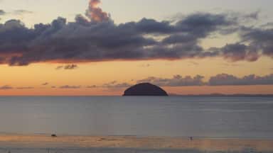 A sunset over a calm sea with a prominent island silhouette and scattered clouds.