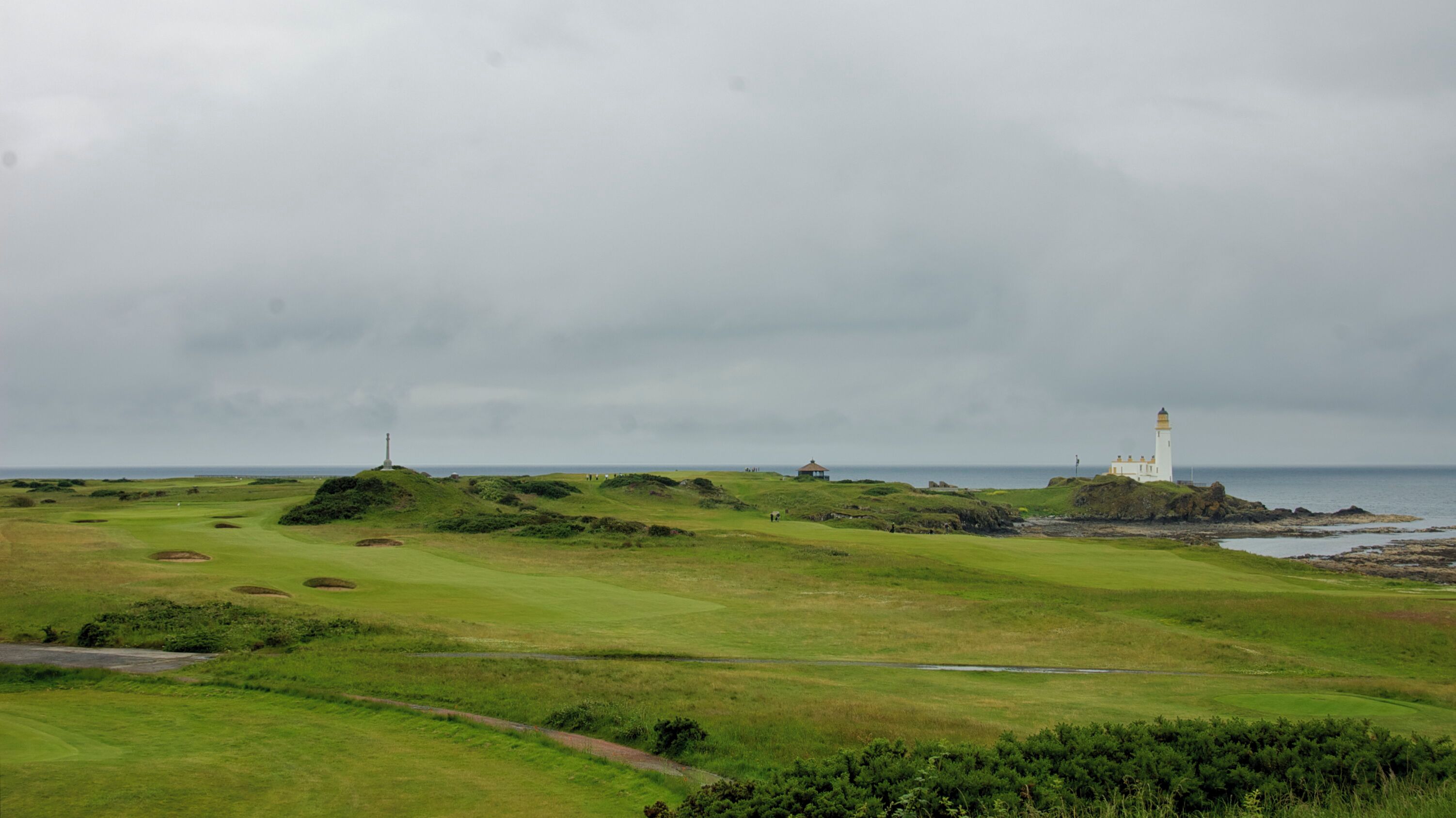 A coastal landscape with a lighthouse, grassy terrain, and a body of water.
