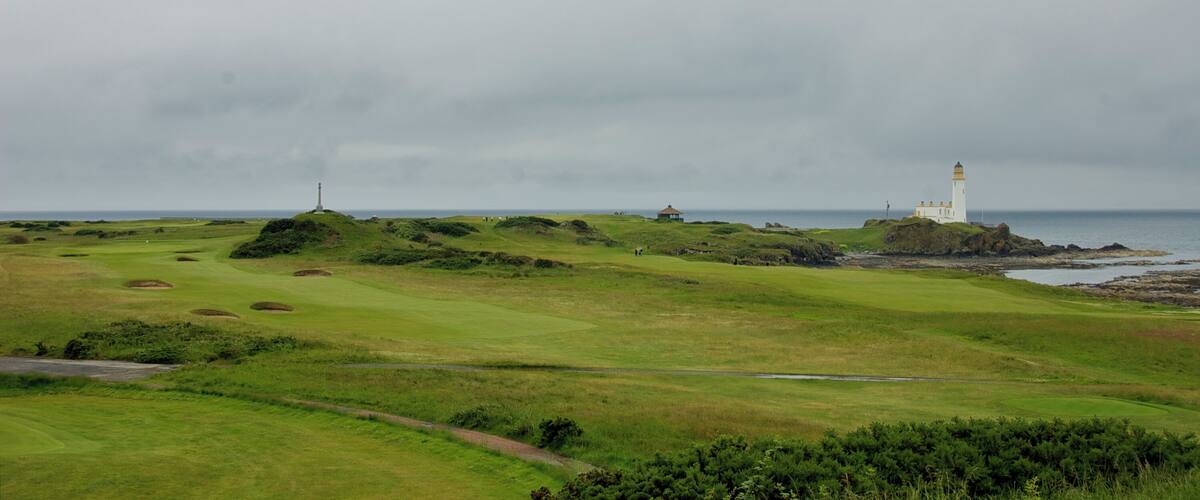A coastal landscape with a lighthouse, grassy terrain, and a body of water.