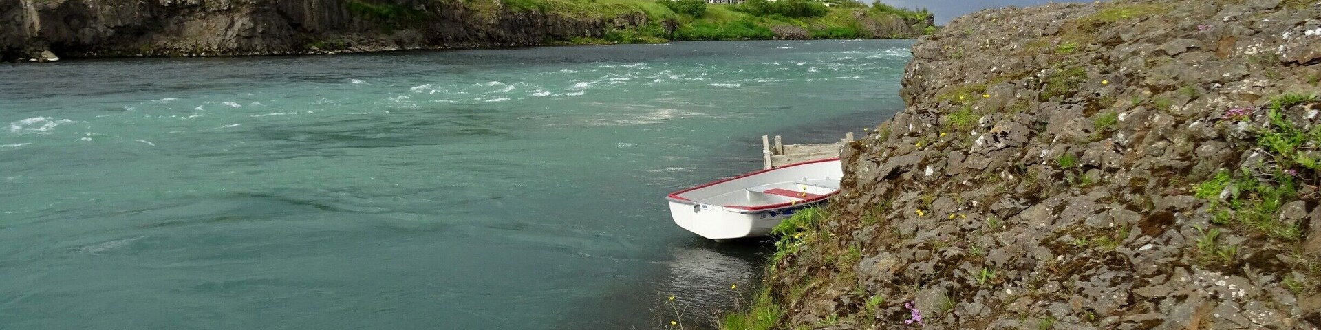 A river with a boat, a rocky shore, and a bridge in the background.
